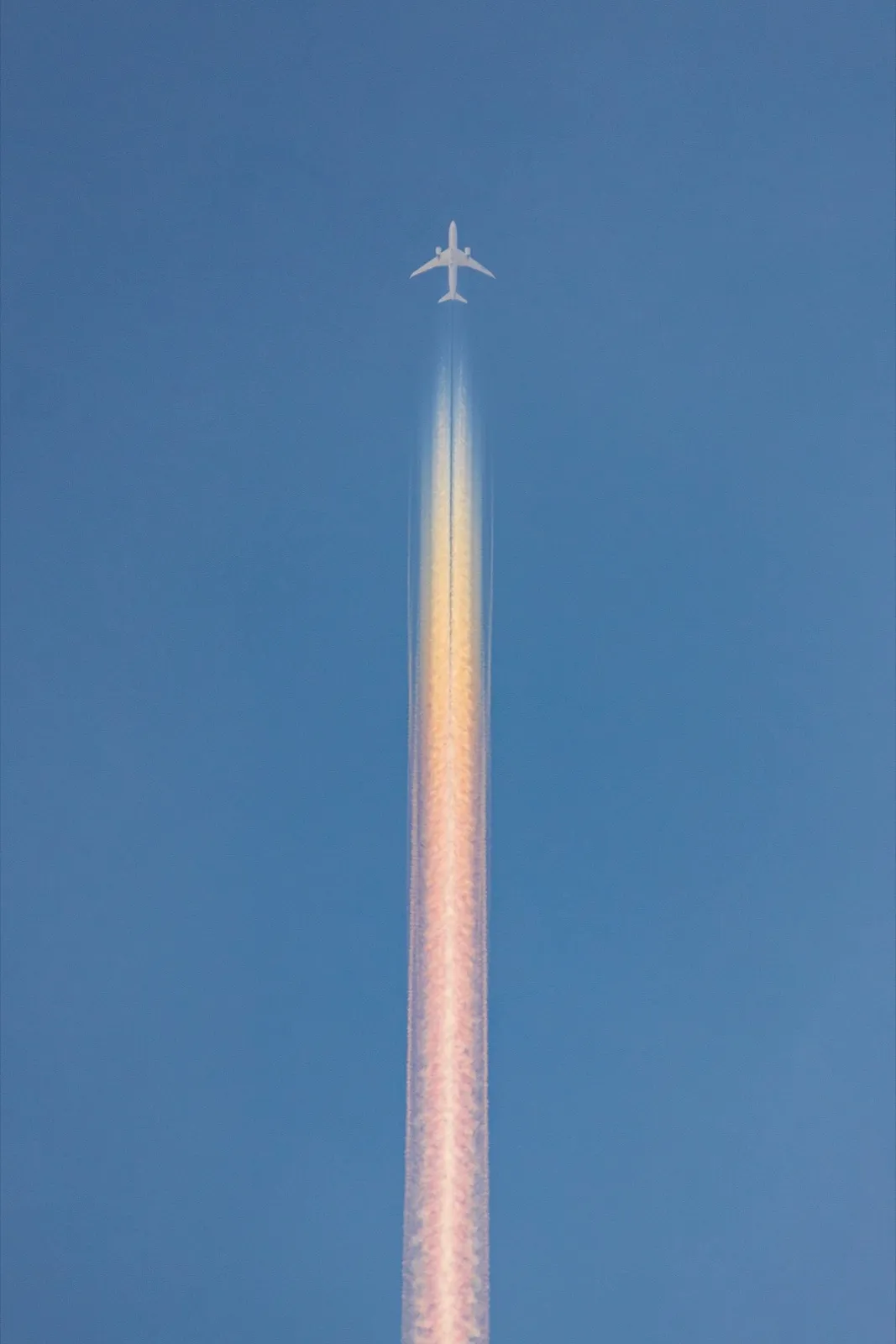 A passenger airplane high in a clear blue sky leaving a long iridescent contrail