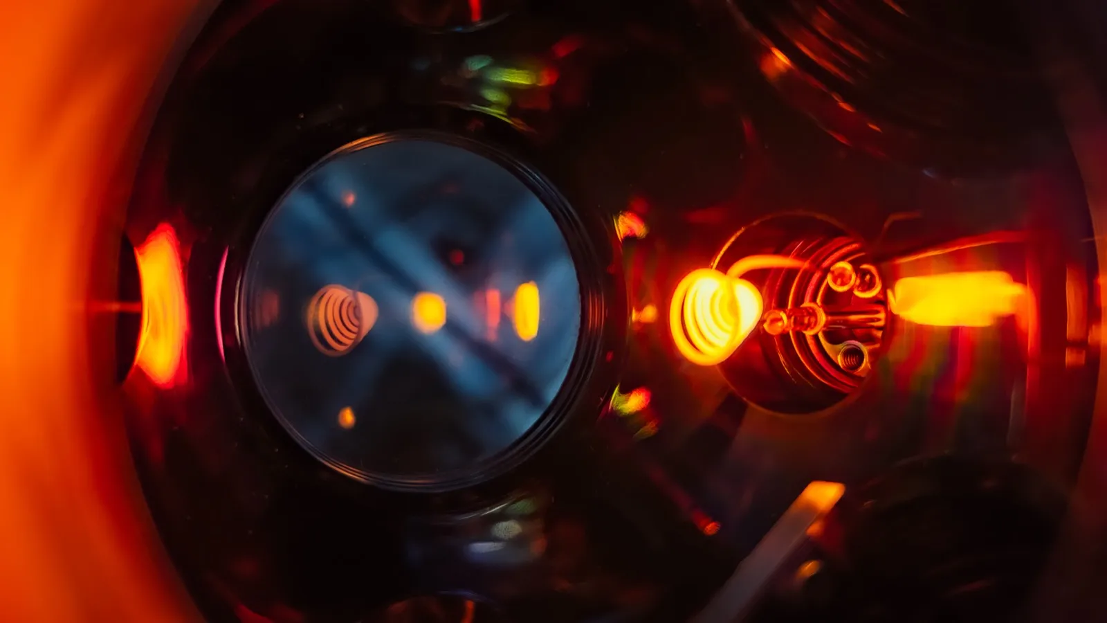 Glowing orange filaments and reflections inside a gold evaporator viewed through a circular window