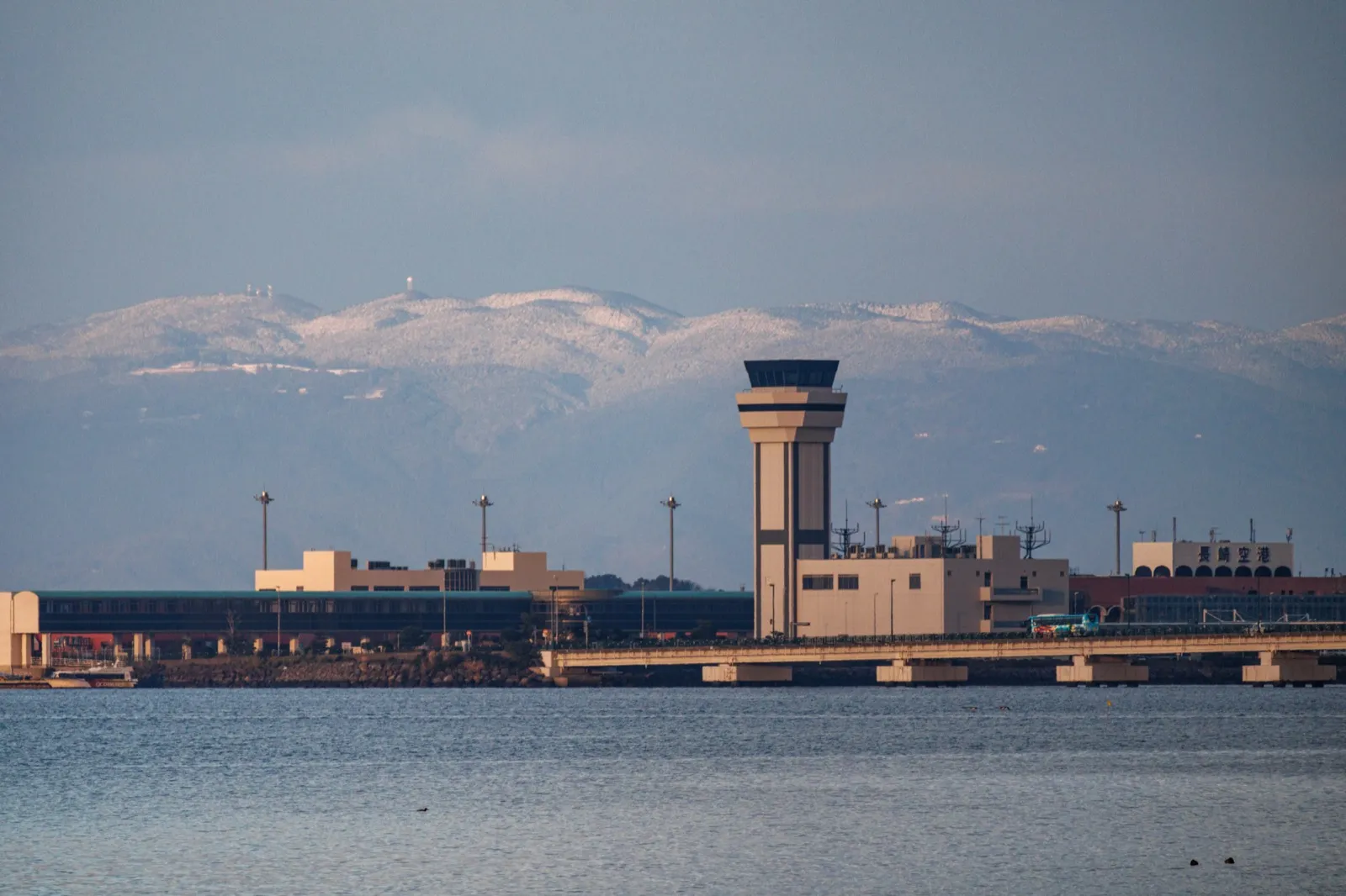 Nagasaki Airport control tower and terminal buildings across calm water with snowy hills behind