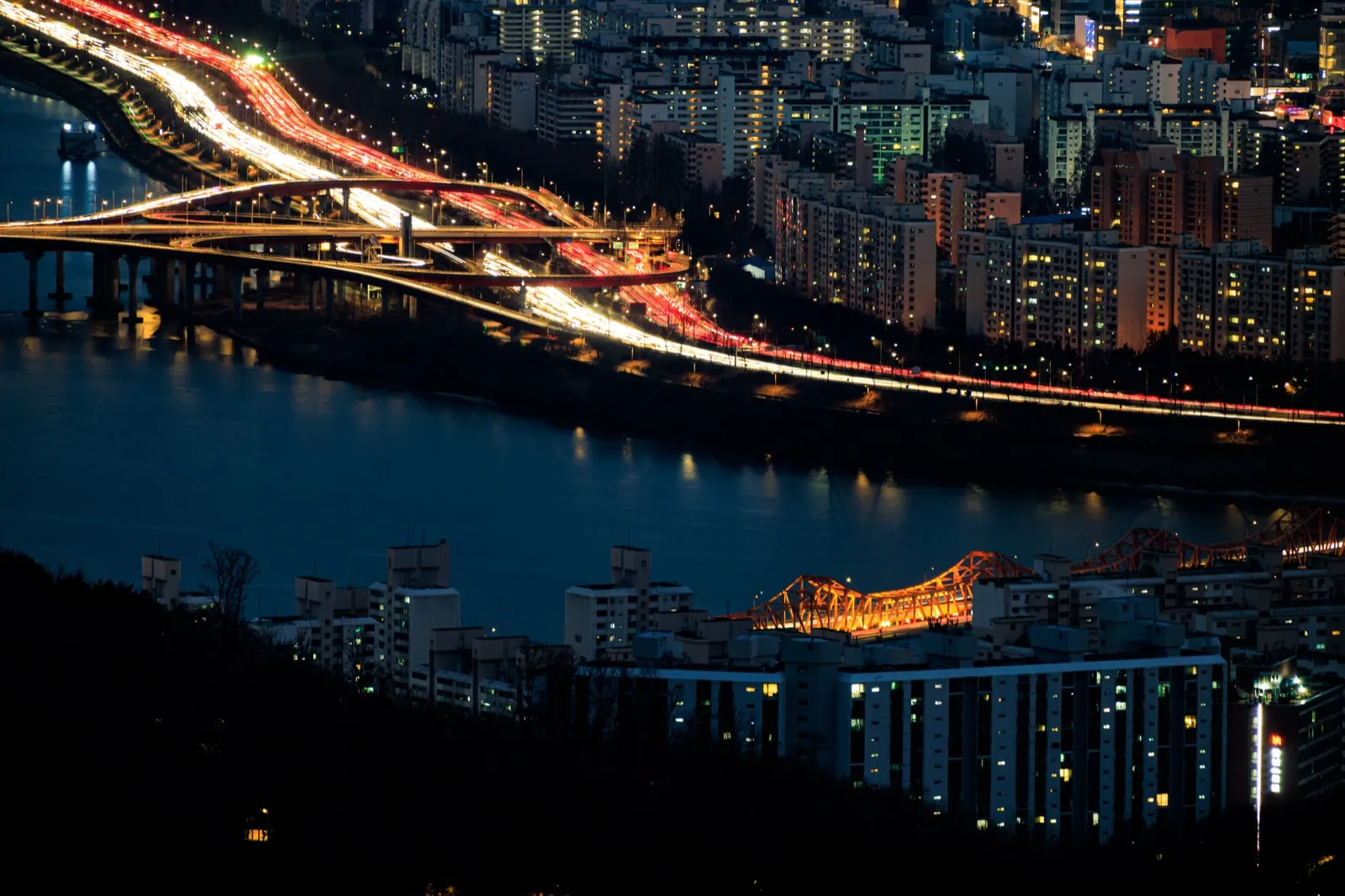 Curving Seoul highways at night with dense streams of white and red traffic lights beside the river